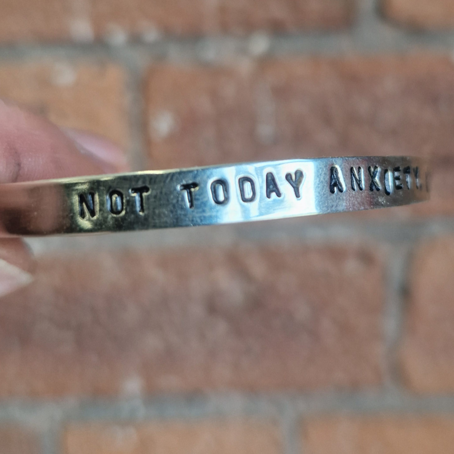 Silver bracelet with 'Not Today Anxiety' text held against a brick wall.