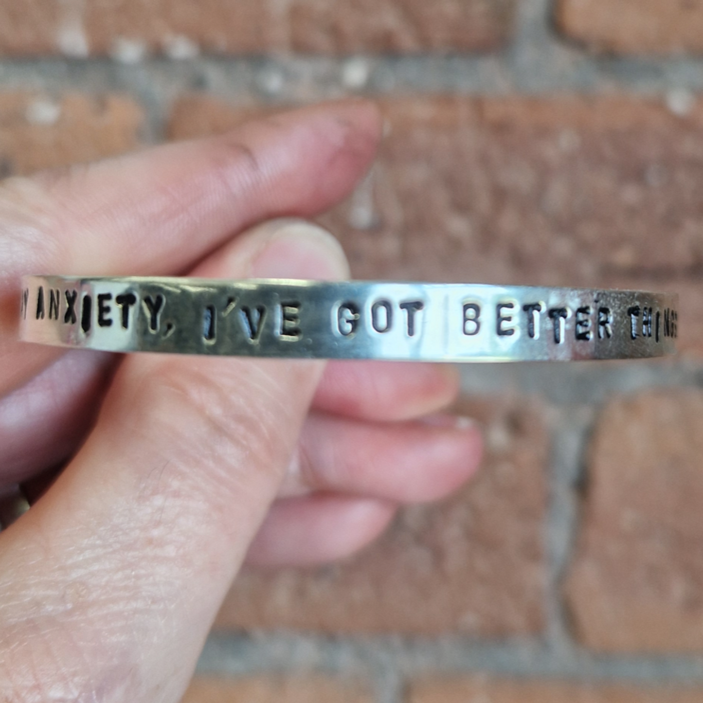 Hand holding a silver bracelet with text against a brick background