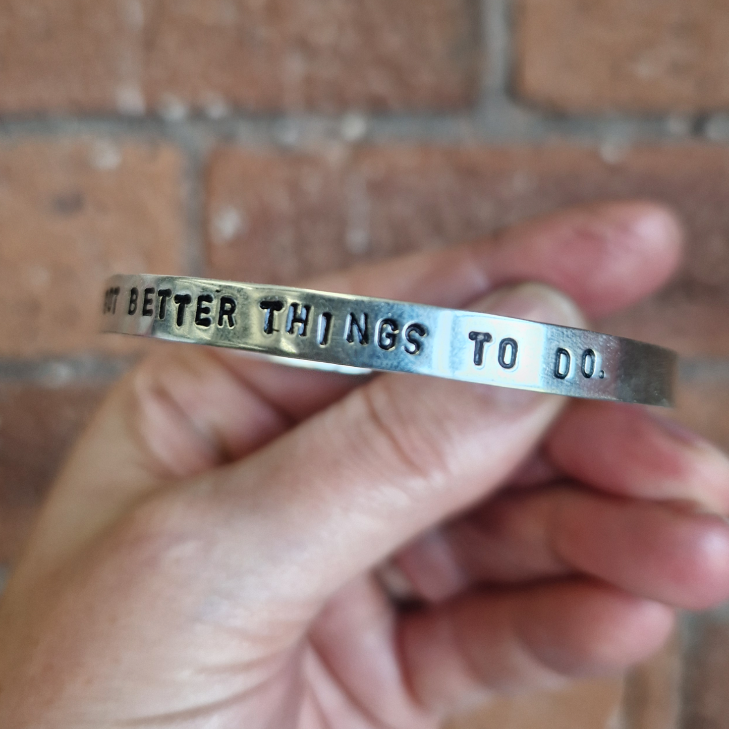 Hand holding a silver bracelet with engraved text against a brick wall background